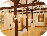 Brightly lit Norman Cross Gallery in Peterborough featuring exposed wooden beams and art pieces lining the walls. 