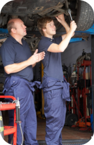 An apprentice mechanic receiving help from a senior colleague 